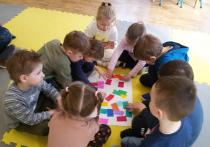 Widok na grupę dzieci zgromadzonych wokół białego kartonu z kolorowymi karteczkami.